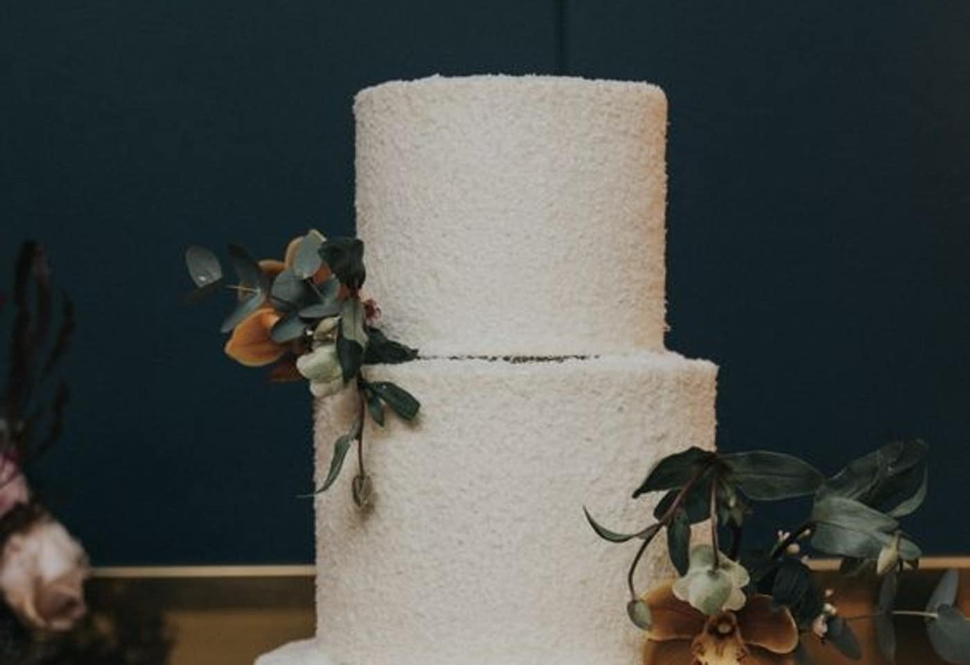 Two-tier textured buttercream custom cake styled with orchids and eucalyptus